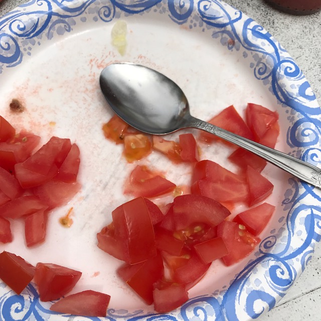 Photo of diced tomatoes scattered across a disposable plate with a serving spoon