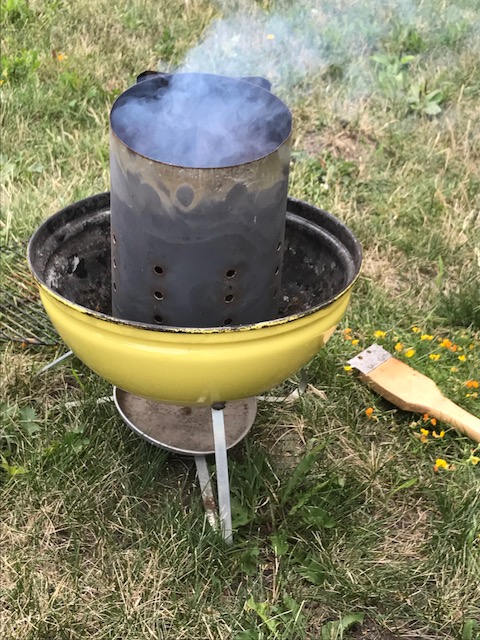 Photo of a small yellow grill with a smoking charcoal chimney