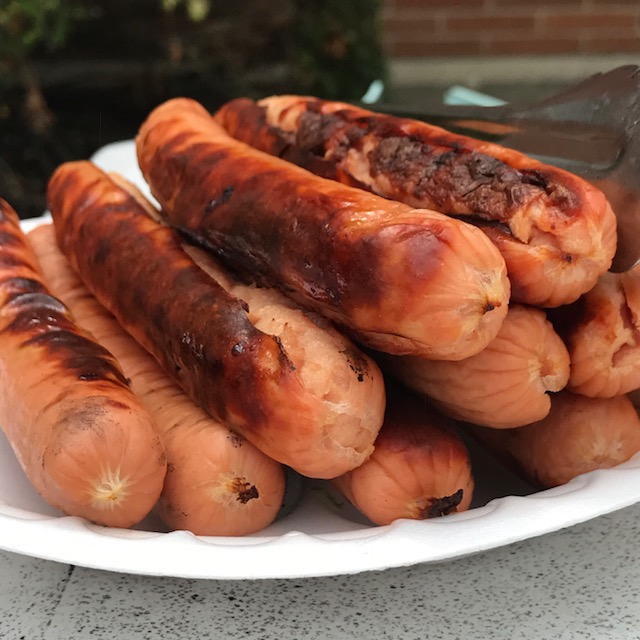Photo of grilled hot dogs stacked on a disposable plate