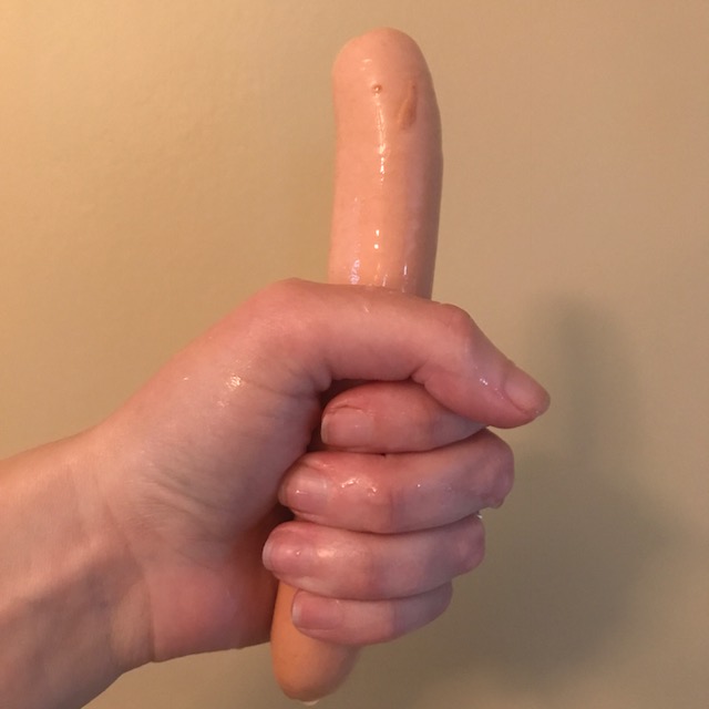 Wet hand gripping a raw wet hot dog